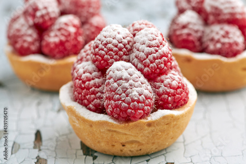 Set of appetizing raspberry tartlets with icing sugar on a spongy sponge base on a wooden table.