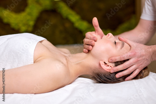 Young woman lying on massage table and enjoying massage by professional masseur, cropped therapist doing healthy massage on neck for female client