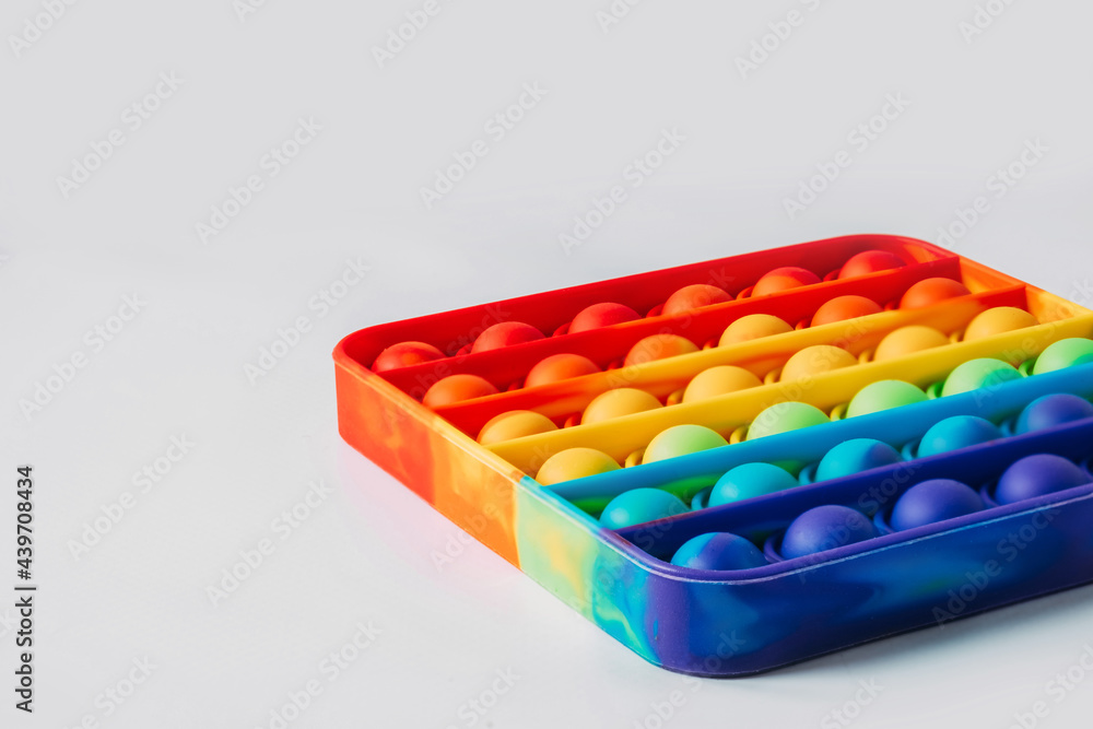The square-shaped pop it anti-stress toy lies sideways. Rainbow touch fidget isolated on white background. New fashionable silicone toy. The square-shaped pop it anti-stress toy lies sideways. Rainbow touch fidget isolated on white background. New fashionable silicone toy.