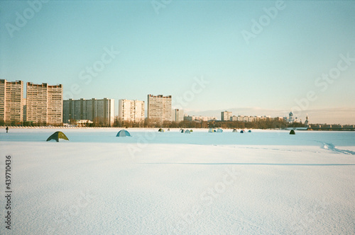 Fishermen tents over a frozen river with soviet architecture buildings behind it photo