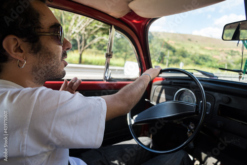 Man wearing a white t-shirt and sun glaces drives a red vintage car in the highway photo