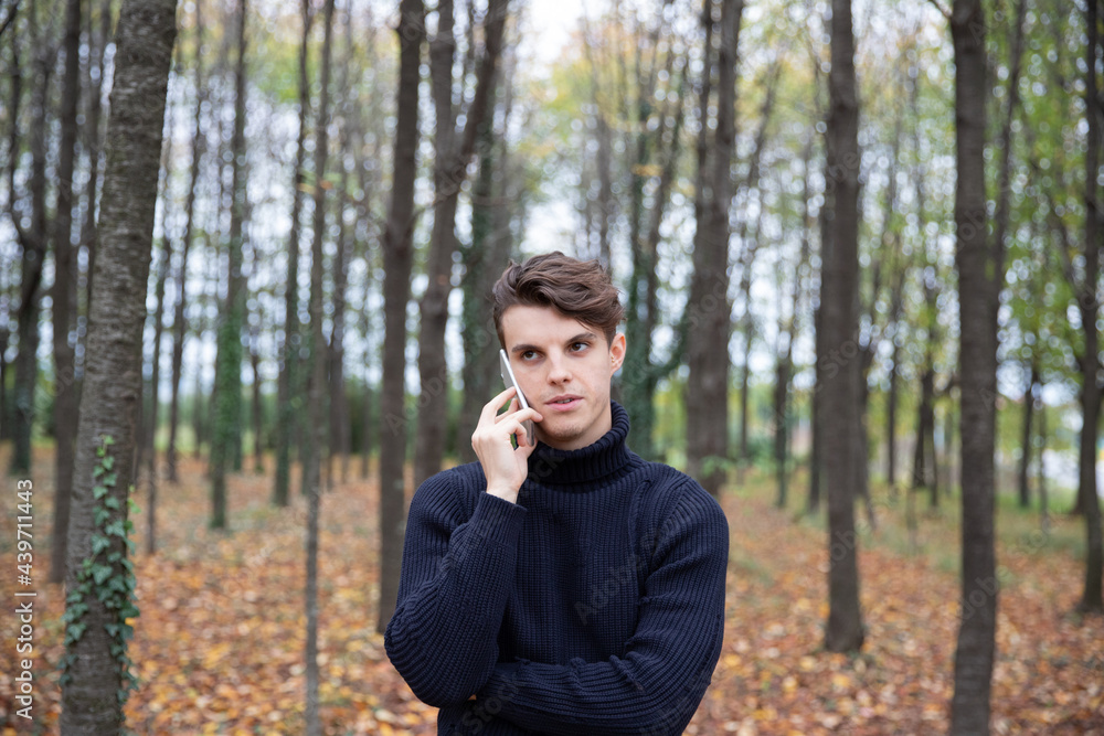 A man in a forest during autumn makes a phone call, all the leaves on the trees are yellow and many leaves have fallen to the ground. A man in a forest during autumn makes a phone call, all the leaves on the trees are yellow and many leaves have fallen to the ground.