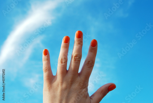 Female hand with orange color manicure on sky background