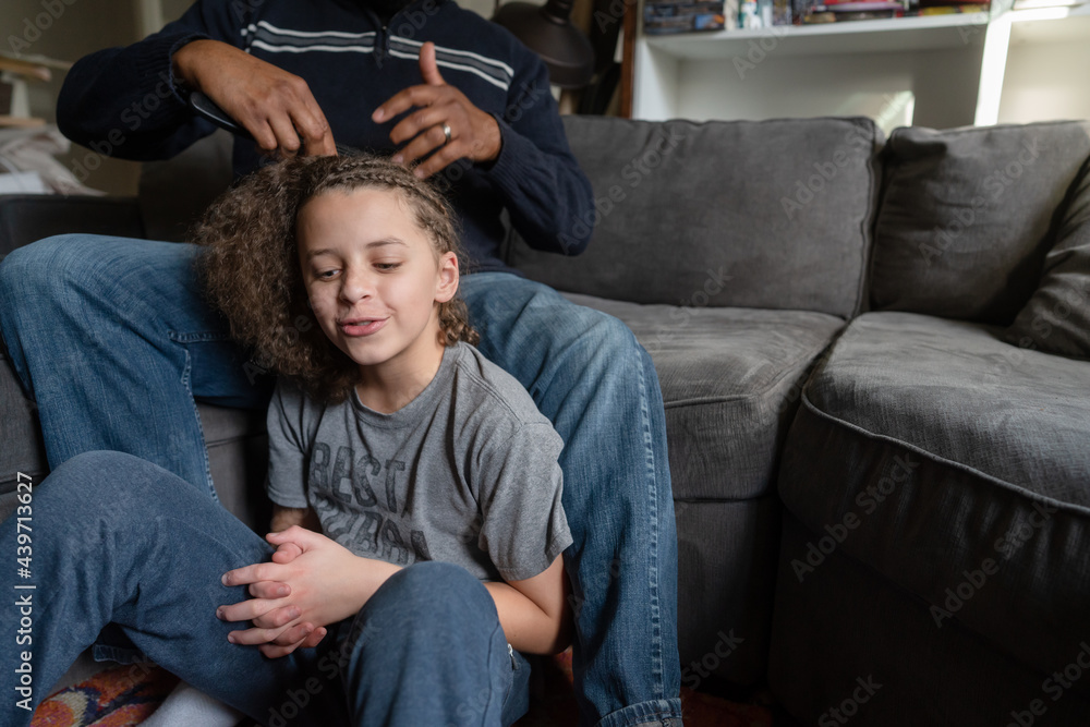 Boy sits at father's feet having hair unbraided Boy sits at father's feet having hair unbraided