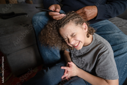 Boy winces in pain as father picks out cornrows photo
