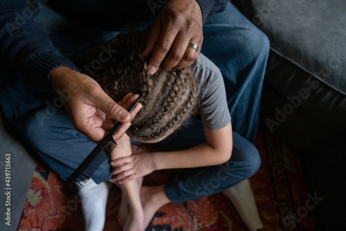 Black dad carefully picks out cornrows on son's hair