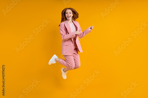 Successful business woman in suit jumping pinting index finger at side, isolated on yellow background, shopping. portrait. copy space photo