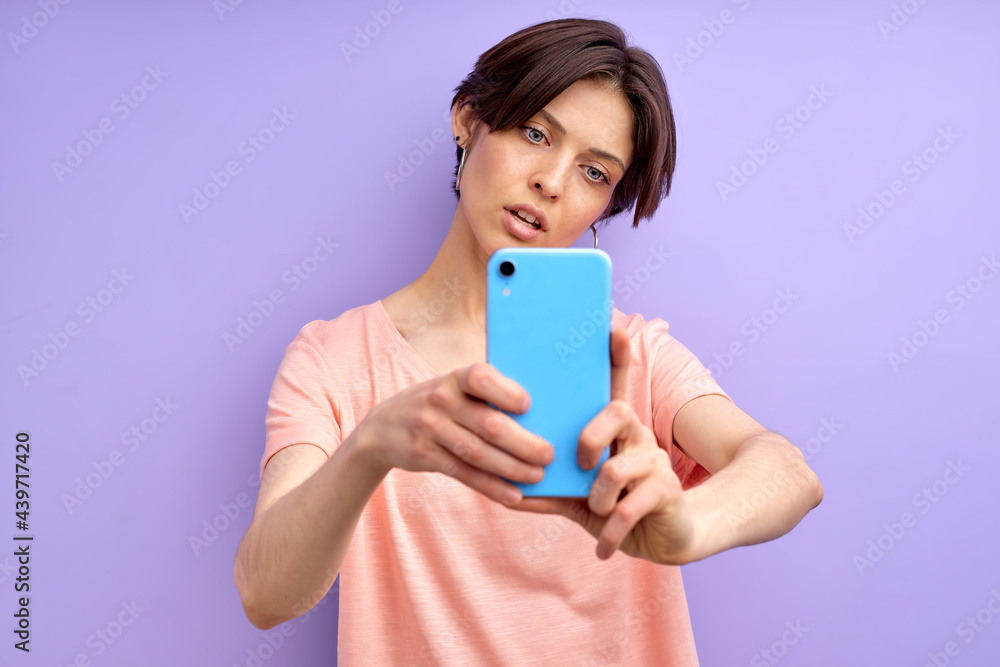 Female model making doing selfie on mobile phone, blogging. Good-looking female with short hair looks at phone's camera and posing, wearing casual outfit Female model making doing selfie on mobile phone, blogging. Good-looking female with short hair looks at phone's camera and posing, wearing casual outfit
