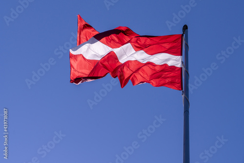 The flag of Latvia waving in the wind against the skylight of the sun on a background of the sky