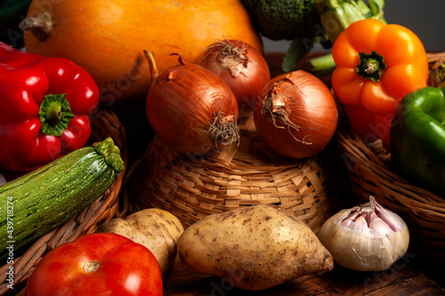 Still life of fresh vegetables on wooden table with wicker baskets, squash, bell peppers, broccoli.