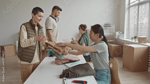 Medium slowmo of young female volunteers giving clothes and food in tins to people coming to their nonprofit charity organization photo