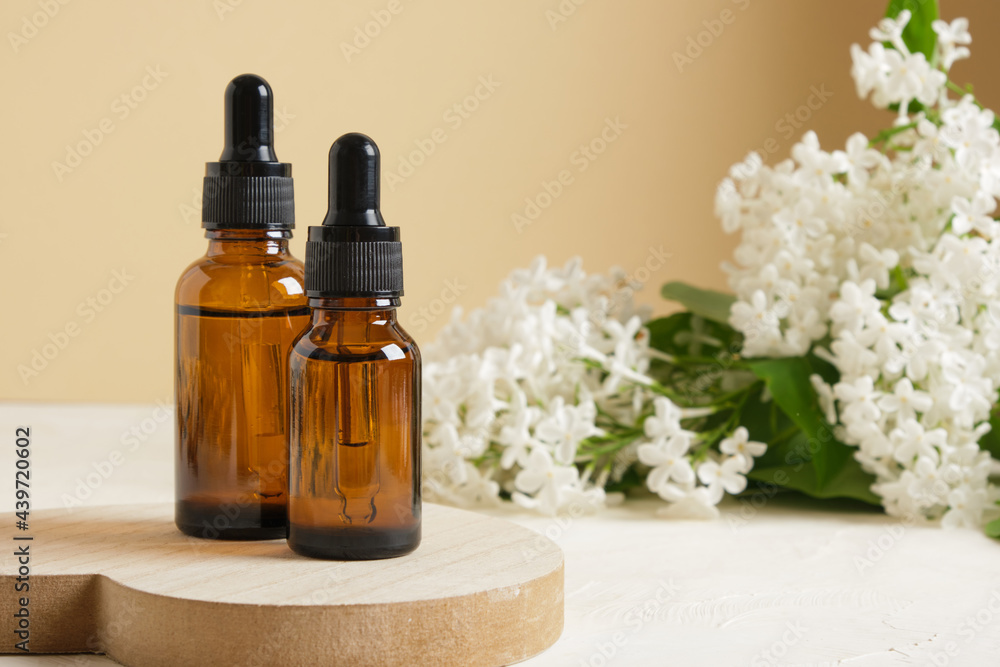 brown bottle with a dropper for cosmetic oils or serums and a branch of white lilac on a beige background brown bottle with a dropper for cosmetic oils or serums and a branch of white lilac on a beige background