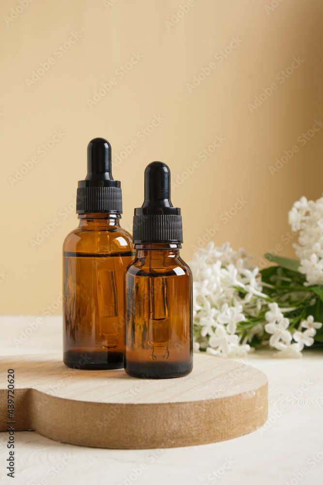 brown bottle with a dropper for cosmetic oils or serums and a branch of white lilac on a beige background brown bottle with a dropper for cosmetic oils or serums and a branch of white lilac on a beige background