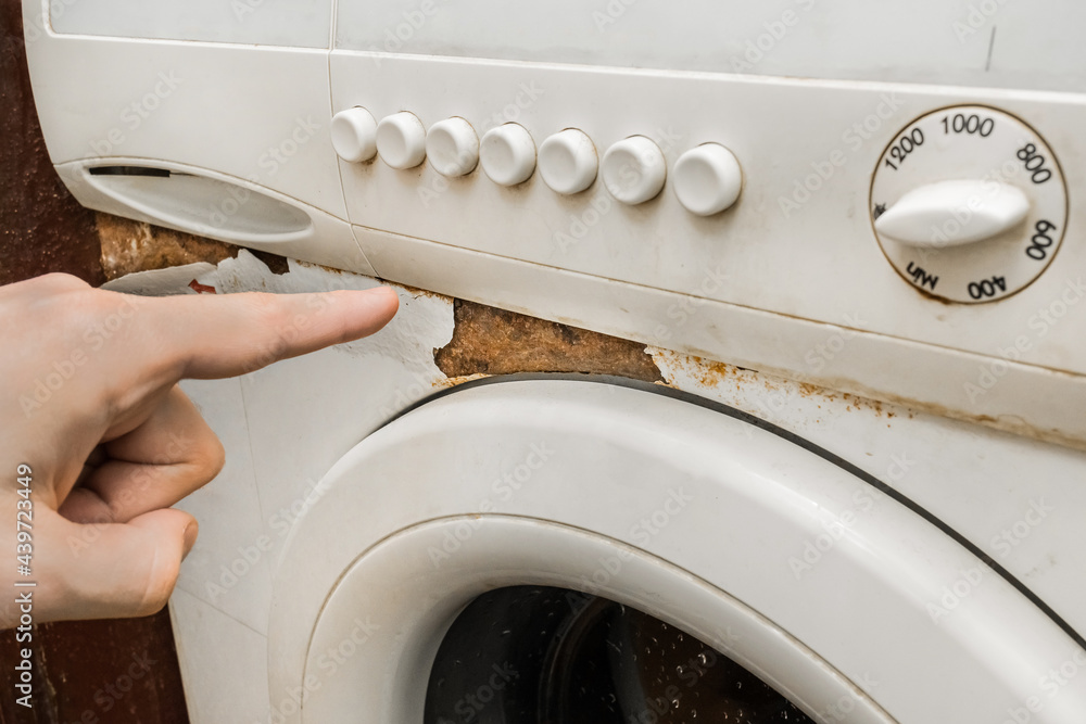A man's hand points a finger at a trace of rust next to the front keypad of an old broken washing machine. Home appliances wear concept A man's hand points a finger at a trace of rust next to the front keypad of an old broken washing machine. Home appliances wear concept