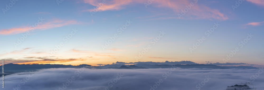 Panoramic beautiful misty morning mountain peaks with orange blue gradient of dawn sky.