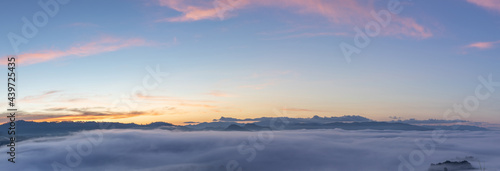 Panoramic beautiful misty morning mountain peaks with orange blue gradient of dawn sky.