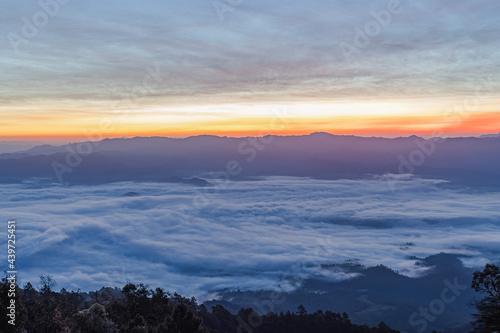 Mountain peaks in morning fog - foggy with orange blue gradient of dawn sky. © AungMyo