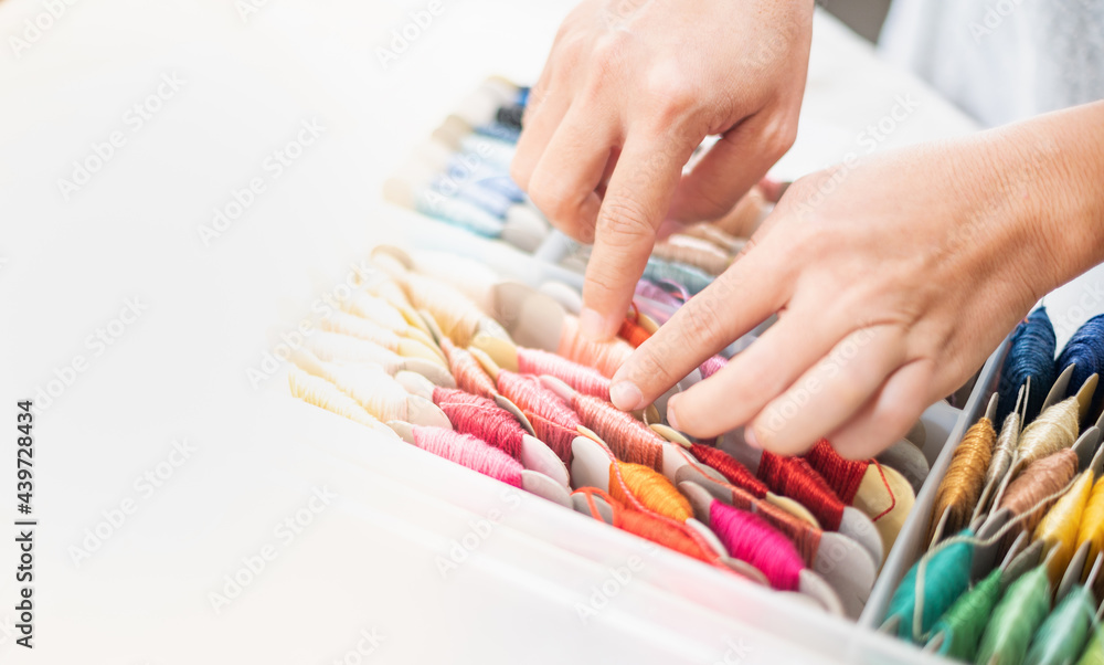 Close up hands of tailor woman choosing different colors thread in the box put on the table and prepare to use with white cotton and frame wood. Close up hands of tailor woman choosing different colors thread in the box put on the table and prepare to use with white cotton and frame wood.