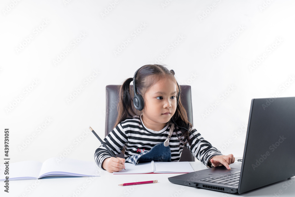 The little Asian girl is focusing on studying hard at home with her notebook with fun, on white background. Concept online learning. The little Asian girl is focusing on studying hard at home with her notebook with fun, on white background. Concept online learning.