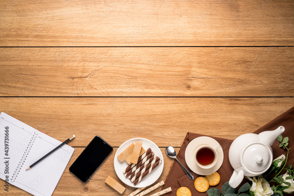 Afternoon tea set with bread, crackers, Wafer, and a mobile phone and a notebook beside on the wooden table, with copy space, top view. Afternoon tea set with bread, crackers, Wafer, and a mobile phone and a notebook beside on the wooden table, with copy space, top view.