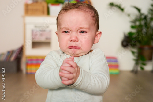 Crying baby holding hands together.
