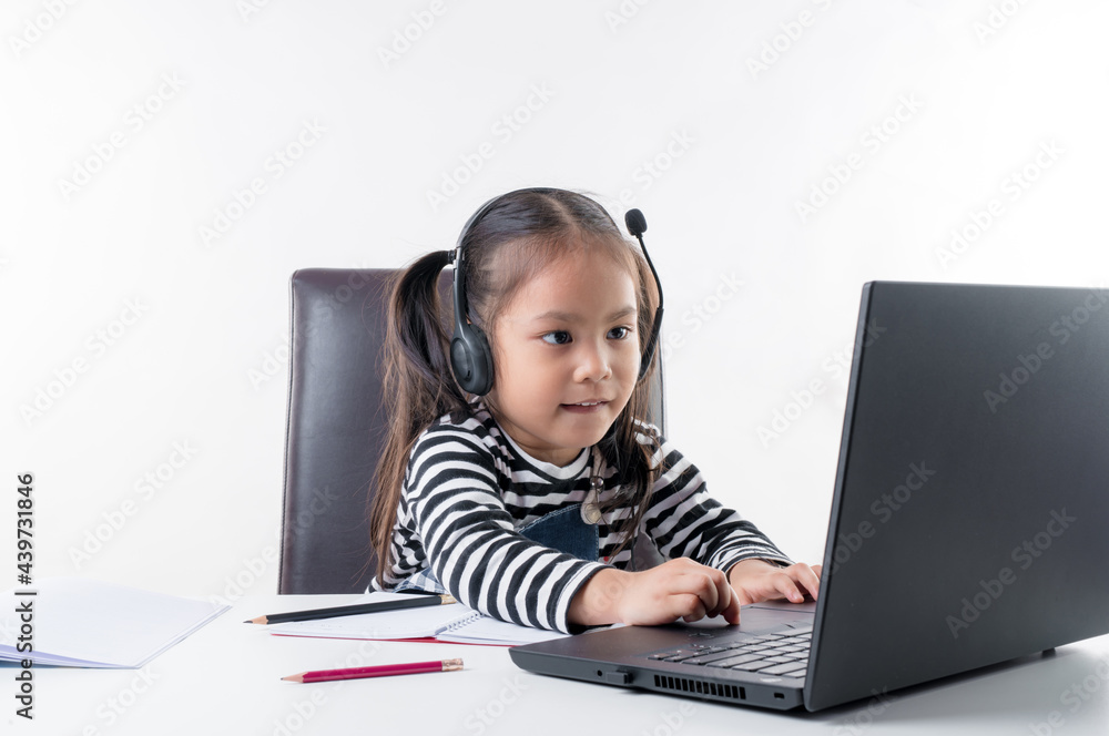The little Asian girl is focusing on studying hard at home with her notebook with fun, on white background. Concept online learning. The little Asian girl is focusing on studying hard at home with her notebook with fun, on white background. Concept online learning.