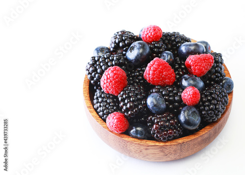 Raspberries  blackberries and blueberries in a wooden bowl on a white background.