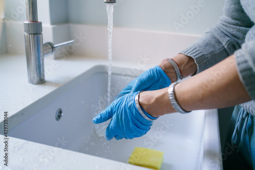 Female hands in blue rubber gloves cleaning container over modern sink photo
