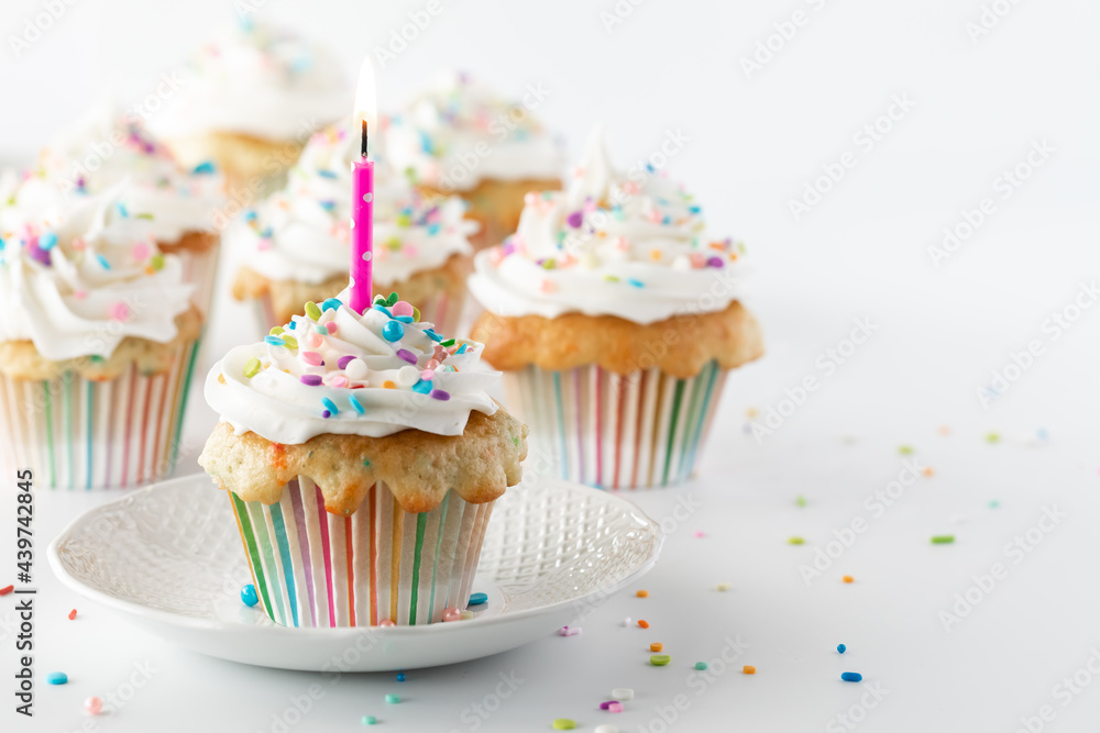 Close up of a cupcake and a lit candle with other cupcakes in soft focus in behind and copy space to the right.