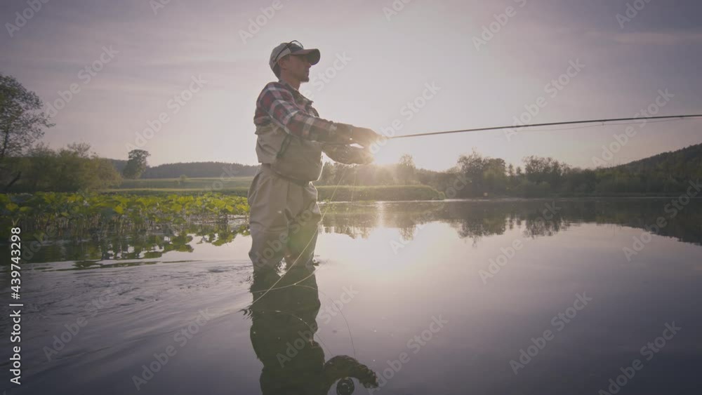 Fly fishing. Angler stands in the river and casts the fly at sunset. Fisherman fishing on fly on the calm river at sunset and casting the line Fly fishing. Angler stands in the river and casts the fly at sunset. Fisherman fishing on fly on the calm river at sunset and casting the line
