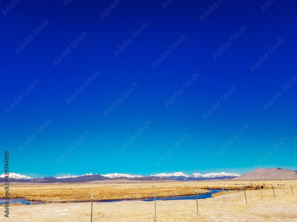 River runs though Arid plain against Sierra Nevada Mountains blue sky 