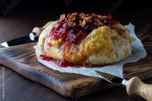 Fotografija Puff pastry wrapped brie topped with cranberry sauce and bacon, ready to be cut into