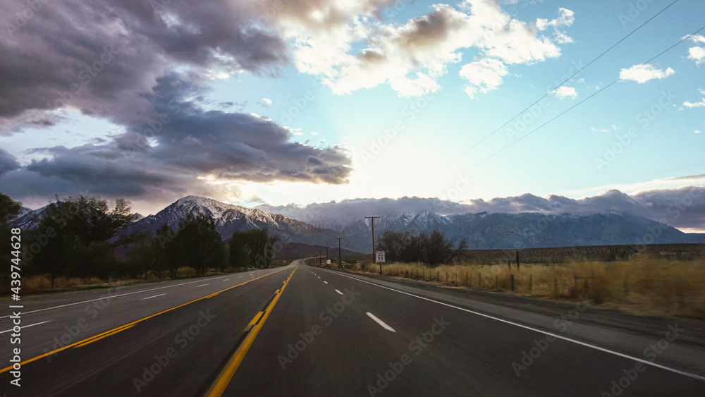road against Dramatic sky and mountains illuminating clouds at sunset