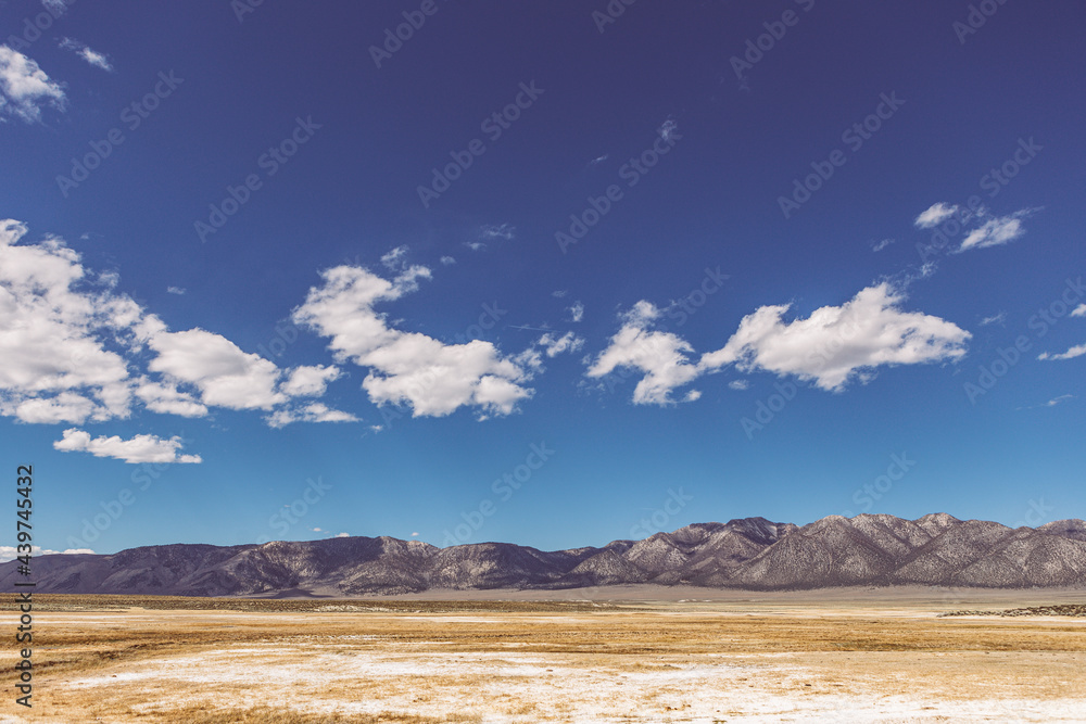 Arid plains against Sierra Nevada Mountains and blue sky with clouds