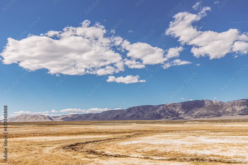 Arid plains against Sierra Nevada Mountains and blue sky with clouds