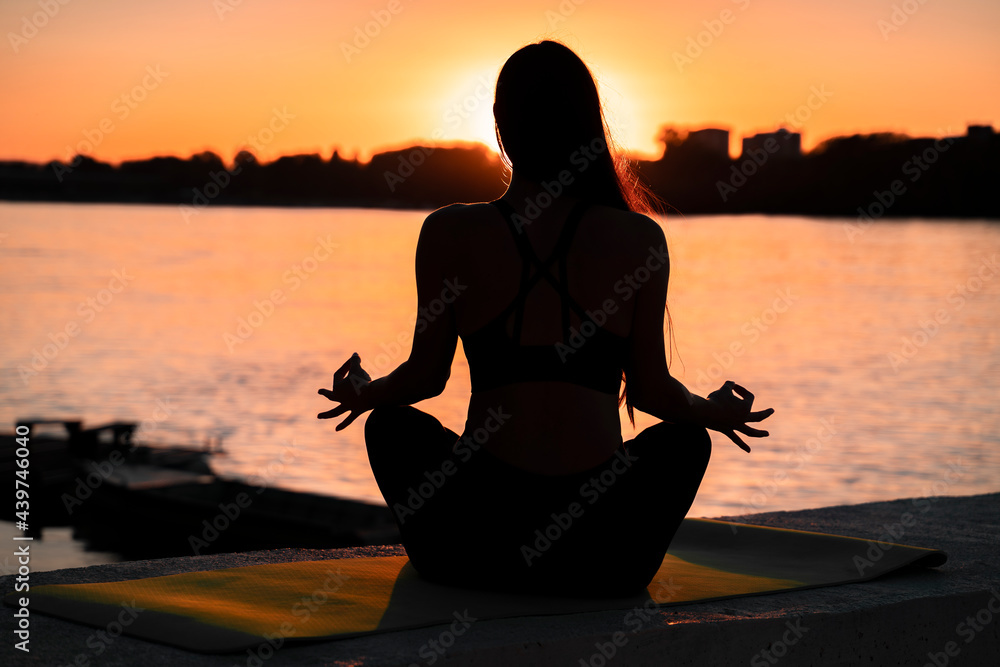 Pretty girl meditating by the river at sunset, silhouette of a girl in meditation 