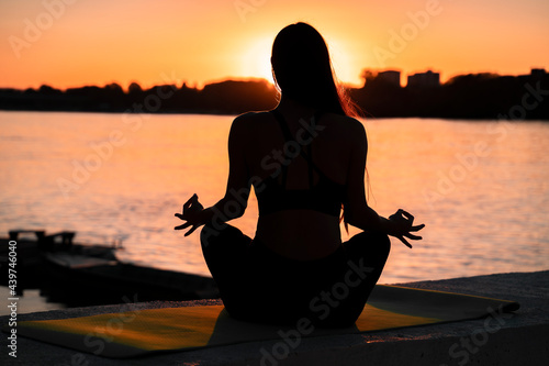 Pretty girl meditating by the river at sunset, silhouette of a girl in meditation 