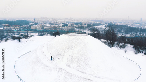 Panoramic view of the Krakus Mound (Kopiec Krakusa) also called Krak Mound. A tumulus located in the Podgórze district of Kraków, Poland. Tourists can be seen standing. Whole area covered with snow. 