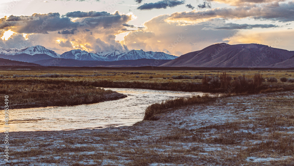 River runs though Arid plain against Dramatic sunset sky and Mountains