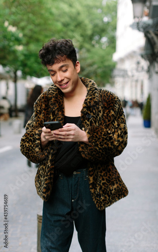 Portrait of young attractive gay man walking in the streets texting on is smartphone photo