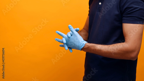 Hands of a man wearing gloves. Dressed in a blue shirt face is not seen in the shot. Yellow background studio. Concept of Covid 19 and precautions. High quality photo. 