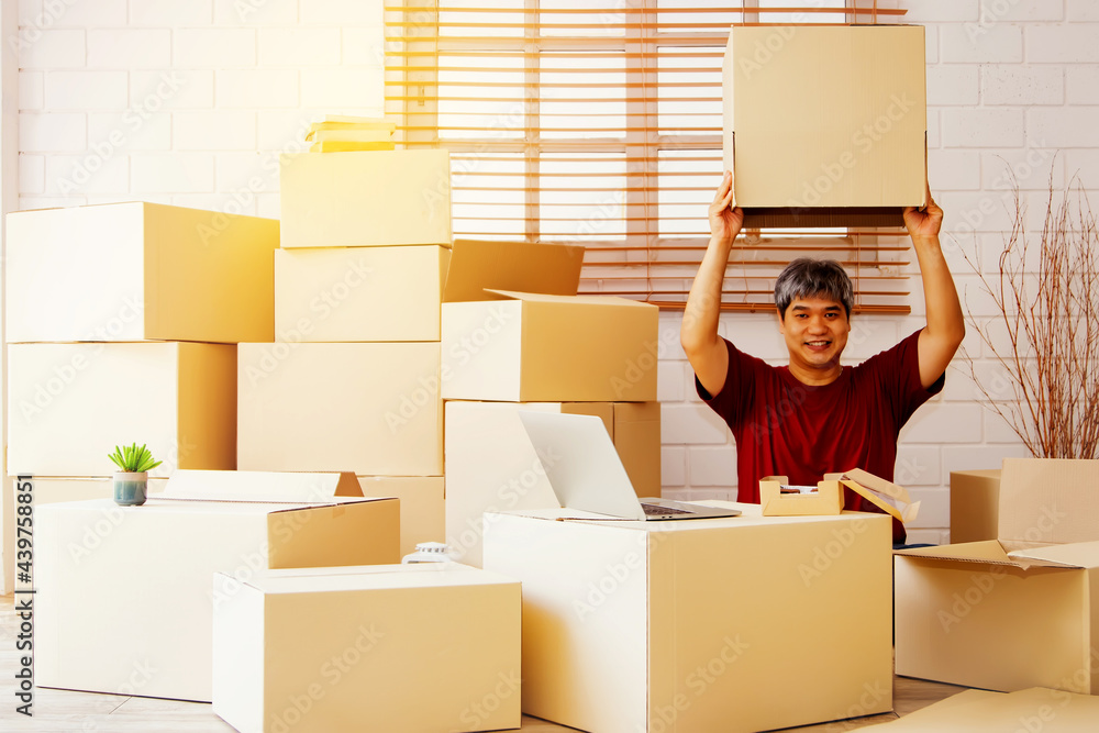 Fototapeta premium Portrait asian guy men sit in the house and there are a lot of boxes in the house : Playful handsome man with an empty box on top of his head is happy with his new home.
