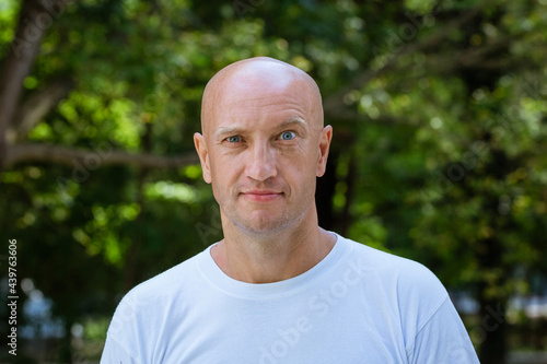 portrait of a bald man in a white T-shirt on the background of the park, mimicry raised eyebrow photo