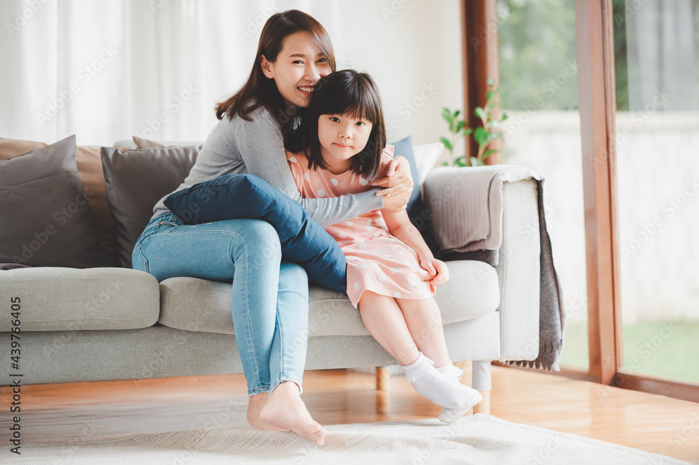 Happy Asian mother and cute little daughter having fun while playing and hugging at home in living room. focused on daughter Happy Asian mother and cute little daughter having fun while playing and hugging at home in living room. focused on daughter
