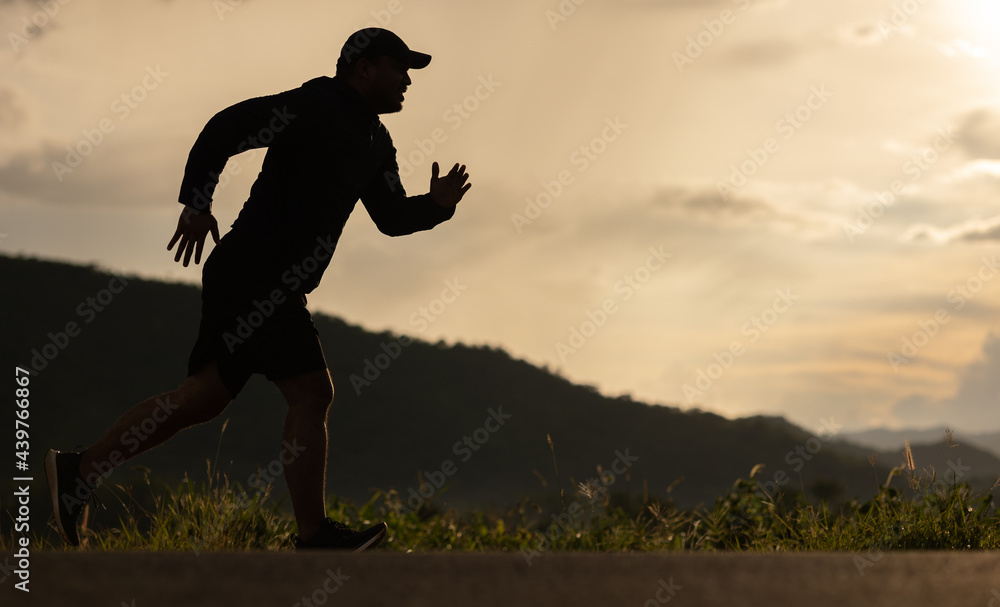 Silhouette Young man wearing sportswear running outdoor nature mountain background. Man jogging on the country side road. Training athlete outdoor concept. Silhouette Young man wearing sportswear running outdoor nature mountain background. Man jogging on the country side road. Training athlete outdoor concept.