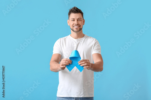 Man with blue ribbon on color background. Prostate cancer awareness concept