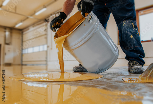 Closeup shot of a construction worker pouring out epoxy resin from a bucket onto a floor photo