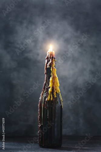 Burning candle with melted wax in a bottle on dark background, halloween decoration
