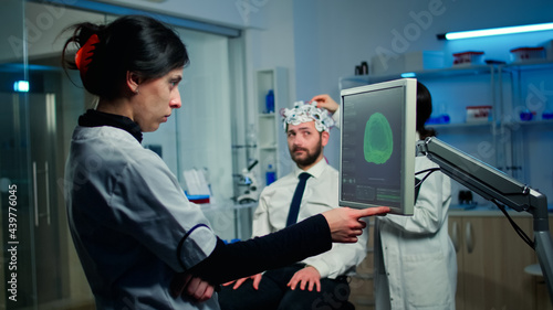 Woman researcher looking at monitor analysing brain scan while coworker discussing with patient in background about side effects, mind functions, nervous system, tomography scan working in laboratory