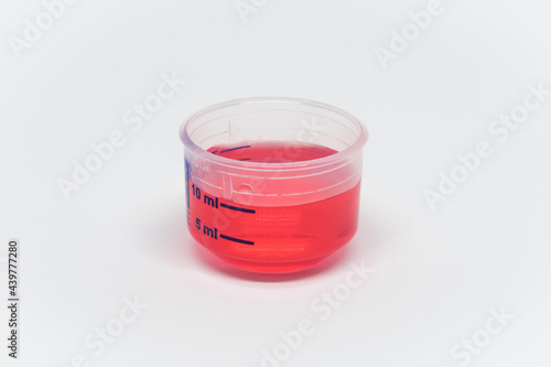 Measuring cup for syrup, cough syrup, medicine, red syrup in cup, white background